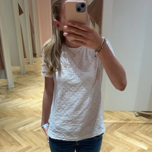 Vit T-shirt med broderade detaljer - Säljer en söt vit T-shirt med broderade detaljer. T-shirten har korta ärmar och ett fint hålmönster . Perfekt för varma dagar eller sommarens fester. Passar bra till både jeans och kjol. Pris kan diskuteras.