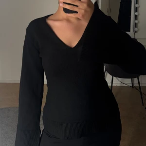 Svart v-ringad stickad tröja - Säljer en stilren svart stickad tröja med v-ringning. Tröjan har långa ärmar och ribbade detaljer vid ärmslut och nederkant.