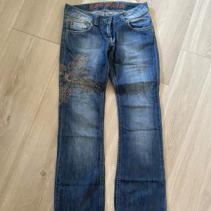 Blå jeans med broderi från Big Star - Snygga blå jeans från Big Star med unikt broderi på ena benet. Midjemått 40cm, ytterbenslängd 100cm.
