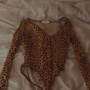 Leopardmönstrad body - Snygg body  med långa ärmar. Perfekt för en djärv och trendig look. Toppen har en omlottdesign som ger en smickrande passform.