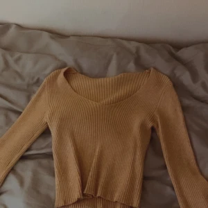 Beige ribbad tröja - Säljer en beige ribbad tröja med lång ärm och croppad design. Perfekt för en stilren och avslappnad look. Tröjan har en rund halsringning och är gjord i ett mjukt material.