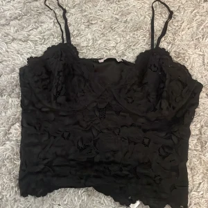Svart spetslinne från H&M - Säljer ett svart spetslinne från H&M med tunna axelband och vacker spetsdetalj. Perfekt för en stilren look. Passar bra till både jeans och kjol.