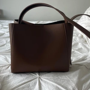 Brun phu bag med dragkedja - Säljer en populär stilren brun axelväska i skinn med både handtag och axelrem som inte längre säljs. Väskan har en rymlig insida med ett innerfack som stängs med dragkedja. Perfekt för dig som vill ha en clean och klassisk look till vardagen. 🥰