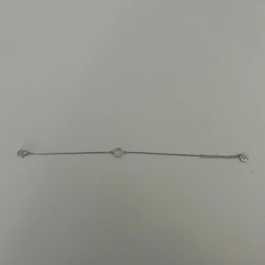 Tunt silverarmband med cirkel - Minimalistiskt armband i silverfärg med en tunn kedja och en enkel cirkelformad detalj i mitten. Perfekt för dig som gillar stilrena smycken. Liten bricka med ingraverad symbol vid låset.