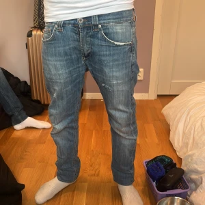 Blå jeans med dragkedjor bak - Säljer ett par blå jeans med snyggt slitna detaljer och dragkedjor på bakfickorna. Jeansen har normal passform och raka ben, klassisk femficksmodell och cool tvätt. Perfekta för dig som gillar en avslappnad men ändå stilren look.