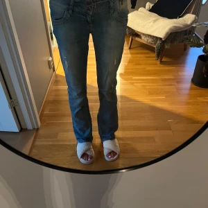 Blå bootcut jeans från LTB - Säljer ett par blå bootcut jeans från LTB med klassisk femficksdesign och slitna detaljer. Jeansen har låg midja och är tillverkade i mjukt denimtyg som ger en avslappnad vibe. Perfekta för dig som gillar en lite retro look. Jeansen är utsydda så att de är mer utsvängda. Midjemått: 40 cm, innerbenslängd: 82 cm🩷