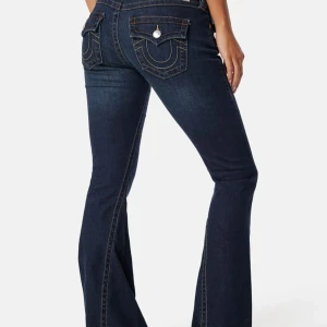 True Religion mörkblå bootcut jeans - Säljer ett par mörkblå bootcut jeans från True Religion i modellen joey lowrise flare med ikoniska kontrastsömmar och snygga fickdetaljer. Jeansen har låg midja och är tillverkade i klassiskt denimtyg. Perfekta för dig som gillar en retro och trendig look. De är lite uppsydda i nedre kanten så passar någon som är 160-165.