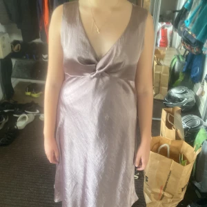 Ljuslila långklänning från Yargici - Säljer en elegant ljuslila långklänning från Yargici. Klänningen är ärmlös med v-ringad omlottfront och har en mjukt skimrande satinliknande yta. Passformen är normal och tyget faller snyggt längs kroppen. Perfekt för dig som gillar stilrena och feminina plagg.