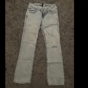 Ljusblå slitna jeans från H&M Divided - Ljusblå jeans från H&M Divided med raka ben och slitna detaljer framtill. Klassisk femficksmodell med broderade bakfickor. Jeansen har normal passform och har en lågmidja.
