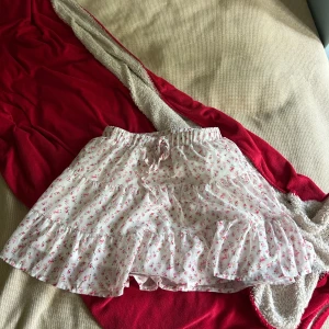 Blommig volangkjol från SHEIN - Supersöt kort kjol från SHEIN med volanger och blommigt mönster i rosa och grönt på vit botten. Kjolen har resår i midjan med snörning och är gjord i mjuk polyester. Perfekt för dig som gillar romantisk och feminin stil.