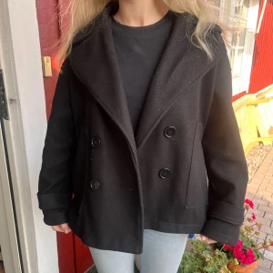 Svart kort kappa  - Stilren svart skepparkavaj med dubbelknäppning och bred krage. Jackan har en loose passform och är tillverkad i 100% polyester, vilket gör den lätt och enkel att bära. Från design by si, nypris 757 kr💕