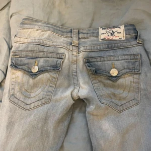 True Religion ljusa bootcut jeans - Säljer ett par ljusblå jeans från True Religion med klassiska bakfickor och snygga kontrastsömmar. Modellen har bootcut-ben 
