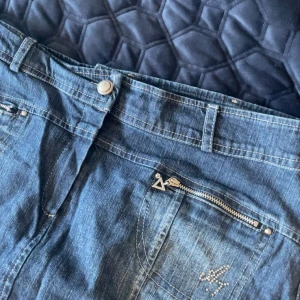 Lång jeanskjol med dragkedjor - Säljer en jättefin blå halvt lång jeanskjol med snygga detaljer som dragkedjor och fickor både fram och bak. Kjolen har bälteshällor och vita sömar. Också någon sorts rhinestone-detalj på framsidan. Den är lite stor så jag brukar använda ett skärp till☺️