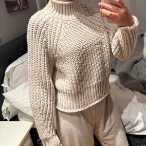 Beige stickad polotröja från H&M - Säljer en chunky beige stickad polotröja från H&M. Tröjan har hög krage, breda ribbade muddar och en loose fit som ger en avslappnad vibe. Perfekt för lager-på-lager och riktigt mysig under kyliga dagar.