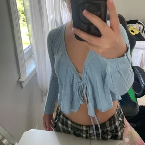 Ljusblå kofta från Stories  - Supersöt ljusblå kofta från Stories i storlek XS. Modellen är croppad med långa ärmar, v-ringning och snygg snörning framtill. Fint skick ❤️