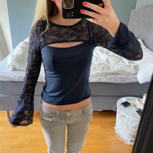 Mörkblå långärmad spetsblus - Säljer en mörkblå blus med långa ärmar i genomskinlig spets och utsvängda ärmslut. Toppen har en snygg cut-out detalj vid bröstet och åtsittande passform. Perfekt för dig som gillar unika detaljer och vill sticka ut lite extra.