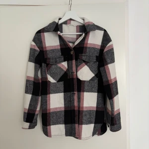 Rutig overshirt i svart, grått och rosa - Snygg overshirt med stora rutor i svart, grått, vitt och rosa. Köpt på H&M. Skjortan har två bröstfickor med lock, klassisk krage och knäppning framtill. Perfekt lager-på-lager-plagg med lång ärm och avslappnad passform.  Storlek 158. Pris kan diskuteras💗