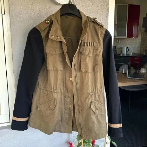 Cool grön höstjacka❤️ - Snygg olivgrön parkajacka med svarta långärmade ärmar och coola detaljer på axlarna. Jackan har flera fickor framtill, dragkedja och knappar. Materialmix med bomull i kroppen och stickade ärmar. Perfekt för dig som vill ha en unik look.