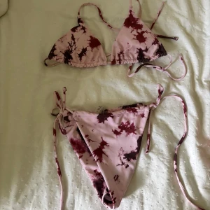 Rosa och vinröd bikini med knyt - Säljer en snygg bikini med rosa och vinröda batikmönster. Överdelen har trekantsform och knyt i ryggen och nacken, medan underdelen har knyt i sidorna. Perfekt för stranden eller poolen i sommar. Materialet är mjukt och följsamt syntet.