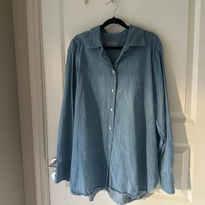 Blå jeansskjorta från Boomerang - Snygg blå jeansskjorta från Boomerang i klassisk modell med krage och knappar framtill. Skjortan är tillverkad i mjukt bomullsmaterial och har långa ärmar. Perfekt oversized fit för en avslappnad look. Köptes för 1499kr i början av sommaren. 