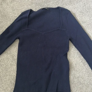 Mörkblå ribbad tröja Gina Tricot - Snygg mörkblå ribbad tröja från Gina Tricot med lång ärm och fyrkantig ringning. Tröjan är figurnära och har diskreta sömdetaljer framtill som ger en cool form. 