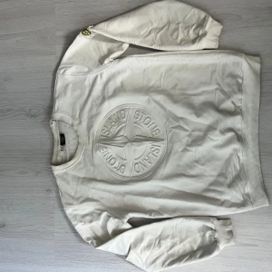 Vit Stone Island sweatshirt med emblem - Säljer en clean vit sweatshirt från Stone Island med stort 3D-emblem på bröstet och klassisk patch på ärmen. Tröjan har rund hals, ribbade muddar och är tillverkad i mjuk bomull. Perfekt för dig som gillar streetwear och vill ha något stilrent med ikonisk logga. Har blivit mindre pågrund av tvätt ! Så ska passa lite tjat 