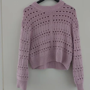 Ljuslila stickad tröja Gina Tricot - Säljer en ljuslila stickad tröja från Gina Tricot i storlek M. Tröjan har ett snyggt hålmönster, ribbade muddar och är lite croppad i modellen. Perfekt att styla med jeans eller kjol för en chill look. Långärmad och mjuk i materialet.Färg Lilla/rosa