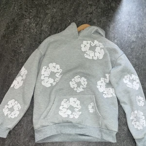 Grå denim tear hoodie ny med tag - Snygg grå hoodie med unika vita mönstertryck över hela tröjan. Tröjan har huva, magficka och är tillverkad i mjuk bomullsblandning. Perfekt för dig som gillar streetwear och vill sticka ut med en cool design.