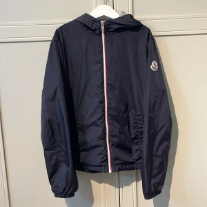 Monclear windbreaker 12y - Säljer nu min windbreaker då jag vuxit ur den. Har använt den en del så skulle säga att skicket är 7/10. Den är perfekt nu till tidig hösten när det börjar bli lite svalare.                          Nypris: 3 500kr.                                                Vid snabb affär kan prisen diskuteras!                                     (Tyvärr är den markerad vi loggan i nacken för igenkänning vid eventuell stöld m.m, dock inget som syns vid användning)