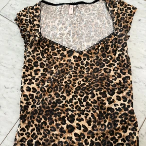 Leopardmönstrad v-ringad topp - Snygg v-ringad topp från Nelly med leopardmönster i bruna och svarta toner. Toppen har korta ärmar och är tillverkad i ett mjukt, stretchigt material som sitter skönt på kroppen. Perfekt för dig som vill sticka ut med ett djurmönster.