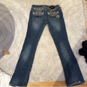 Miss me bootcut jeans - Snygga Lågmidjade blå jeans från Miss Me med blingade detaljer och broderier på bakfickorna. Jeansen har bootcut-modell, låg midja och coola nitar och stenar som ger extra edge. Perfekta för dig som vill sticka ut med din stil. en knapp är utbytt