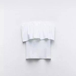 Vit bandeau tubtopp med volang - Supersnygg vit bandeau tubtopp med bred volang upptill som ger en cool och trendig look. Toppen är axelbandslös och har en clean, stilren design som passar perfekt till sommarens outfits. Materialet känns mjukt och följsamt mot huden.