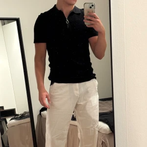 Svart pikétröja med dragkedja H&M - Svart pikétröja från H&M i slim fit med kort ärm och krage. Tröjan har en ringformad dragkedja framtill och är tillverkad i ett strukturerat, stickat material.