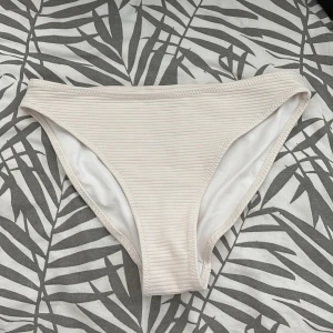 Vit ribbad bikiniunderdel från H&M - Snygg vit bikiniunderdel från H&M i storlek 34. Modellen har en klassisk passform med ribbad struktur och mjukt tyg som sitter skönt. Perfekt för strandhäng eller poolparty. Enkel och stilren design som är lätt att matcha med olika överdelar. Aldrig använd 