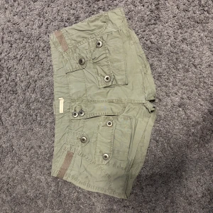 Gröna cargo shorts med fickor - Säljer ett par gröna cargo shorts med låg midja och flera stora fickor med knappar fram och bak. De har en loose passform. Har sytt om shortsen från ett par större shorts och kan därför ha lite skakiga sömmar. Skeiv om du har frågor, pris är diskuterbart! ❤️