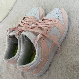 Nike Dunk Low i vitt och ljusrosa - Snygga Nike Dunk Low sneakers i vitt och ljusrosa, 