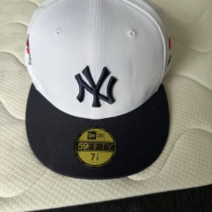 NY Yankees 59FIFTY keps vit/svart - Snygg New Era 59FIFTY keps med New York Yankees-logga framtill. Kepsen är vit med svart skärm och broderad World Series-detalj på sidan. Klassisk flat brim och grön undersida på skärmen. Perfekt för dig som vill sticka ut med sportig stil.