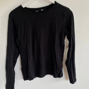 Svart långärmad tröja i bomull - En enkel svart långärmad tröja i mjuk bomull. Modellen har rund halsringning och en normal passform som funkar till allt. Perfekt att ha som basplagg och lätt att matcha med andra kläder.