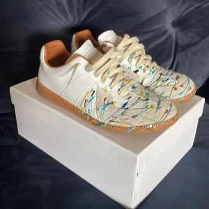 Maison margiela paint splatter - Super snygga Maison Margielas i vitt skinn med färgstänk som gör de unika. Skorna är super sköna och skornas skick är mycket bra skick nästan ny skick. Perfekt för dig som vill sticka ut med en kreativ och trendig look. Boxen o allt tillkommer med🤗Jag tar även emot byten och de skulle vara så💯