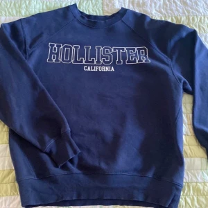 Mörkblå Hollister sweatshirt XS - Snygg mörkblå sweatshirt från Hollister i storlek XS. Tröjan har klassisk rund hals och vit Hollister California-tryck på bröstet. Mjuk och skön bomullsmix med långa ärmar och ribbade muddar. Perfekt för chill dagar!