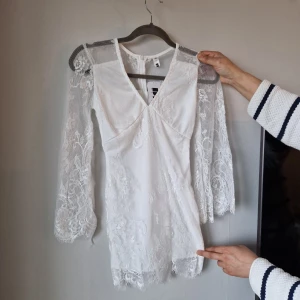 Vit spetsklänning - Elegant vit klänning med v-ringning och långa spetsärmar. Klänningen har en kort längd och är dekorerad med vacker spetsdetaljering. Perfekt som student klänning. Säljer fler klänningar så kika gärna på min profil.