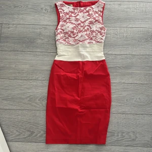 Röd och vit klänning från Vesper - Snygg röd och vit klänning från Vesper med spetsdetaljer på överdelen. Klänningen har en tight passform och är ärmlös, perfekt för festliga tillfällen. Den har en dragkedja i ryggen för enkel påklädning.