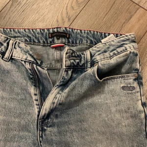 Blå jeans från Tommy Hilfiger - Säljer ett par snygga blå jeans från Tommy Hilfiger. De har en klassisk femficksdesign och en dragkedja framtill. Perfekta för en avslappnad stil med en touch av vintage. Jeansen har en slitning där bak, men den syns inte när man har dem på.