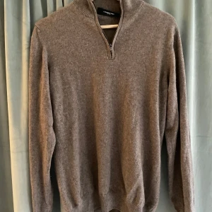 Brun kashmirtröja från Lawrence Grey - Säljer en lyxig brun kashmirtröja från Lawrence Grey. Tröjan har en dragkedja framtill och en hög krage som ger en stilren look. Perfekt för kyligare dagar med sin mjuka och varma känsla. Ett måste för garderoben!