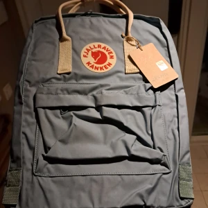 Blå ryggsäck från Fjällräven - Säljer en klassisk blå Fjällräven Kånken ryggsäck. Den har justerbara axelremmar och ett stort huvudfack med dragkedja. Perfekt för både skola och utflykter. Den ikoniska loggan pryder framsidan och ger en tidlös stil. Hör av dig vid intresse!