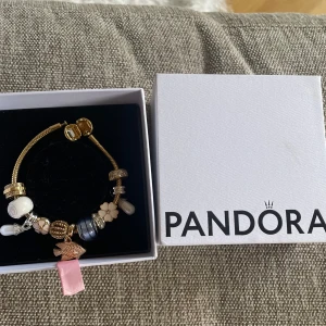 Guldarmband med berlocker från Pandora - Säljer ett elegant guldarmband från Pandora med flera unika berlocker. Armbandet är använt men mycket fint skick, se bilder. 14K guldpläterat, medföljer 7 stycken Pandora berlocker (se bild 3&4) och en hel del andra berlocker från olika ställen (ej Pandora). Storlek 17cm. Tar emot prisförslag! 