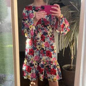 Blommig klänning med volangdetaljer - Säljer en färgglad blommig klänning med volangdetaljer. Klänningen har långa ärmar och ett livfullt mönster i rött, rosa, blått och gult. Perfekt för skolavslutning eller en solig sommardag! 🌸