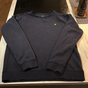 Mörkblå sweatshirt från Lyle & Scott - Säljer en mörkblå sweatshirt från Lyle & Scott Junior. Tröjan har en broderad gul logga på bröstet och är tillverkad i en mjuk bomulls- och polyesterblandning. Perfekt för en avslappnad stil. Kom med förlag ifall priset inte passar och skriv om ni undrar över något 😁