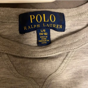 Grå tröja från Ralph Lauren - Säljer en stilren grå tröja från Ralph Lauren med rund hals och det klassiska logotypbroderiet på bröstet. Tröjan har långa ärmar och ribbade muddar vid ärmslut och nederkant. Perfekt för en avslappnad look.