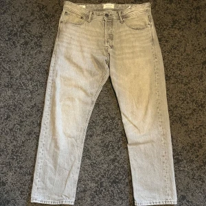 Grå jeans från Jack & Jones - Säljer ett par grå jeans från Jack & Jones i modellen Loose/Chris. De har en regular  passform och klassisk femficksdesign med knappgylf. Perfekta för en avslappnad stil. Storlek 32/30